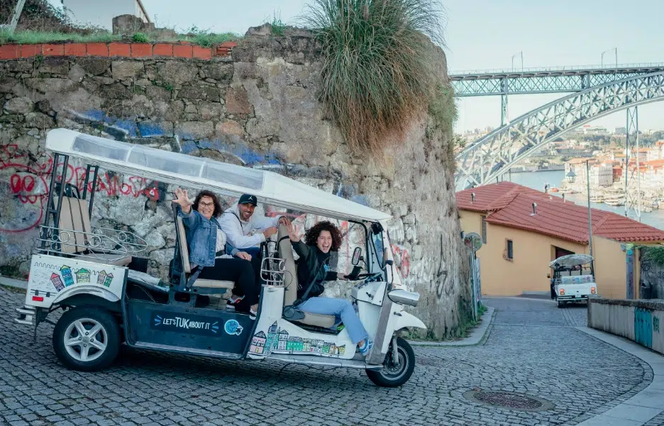 Tuk Tuk on a cobblestone street with Dom Luís I Bridge in Porto