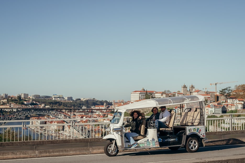 Tuk Tuk driving along a bridge with panoramic views of Porto, Portugal