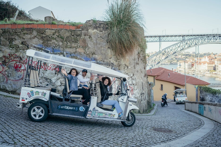 Tuk Tuk on a cobblestone street with Dom Luís I Bridge in the background, Porto