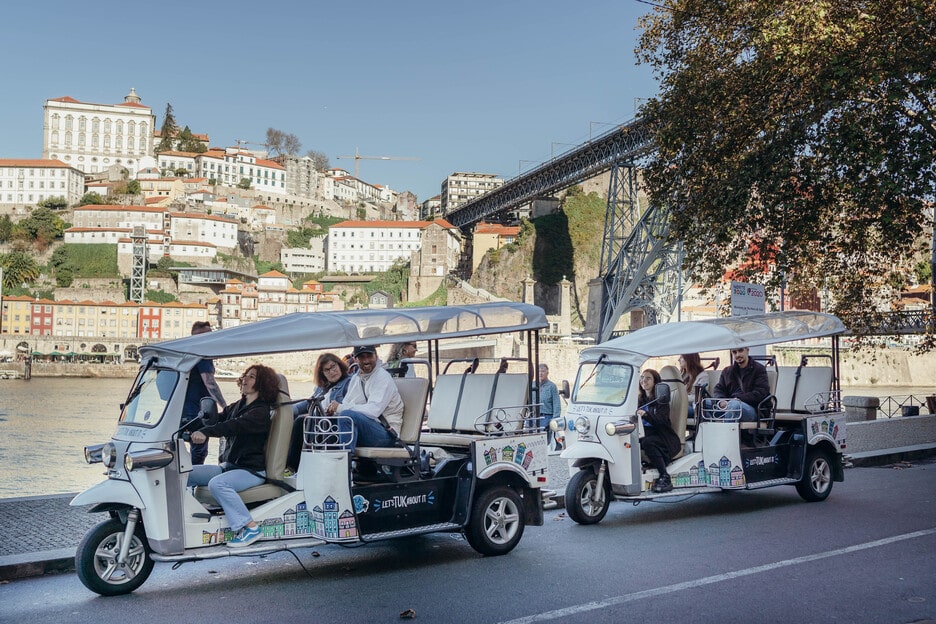 Tuk Tuk tours by the riverside with the Dom Luís I Bridge in Porto, Portugal