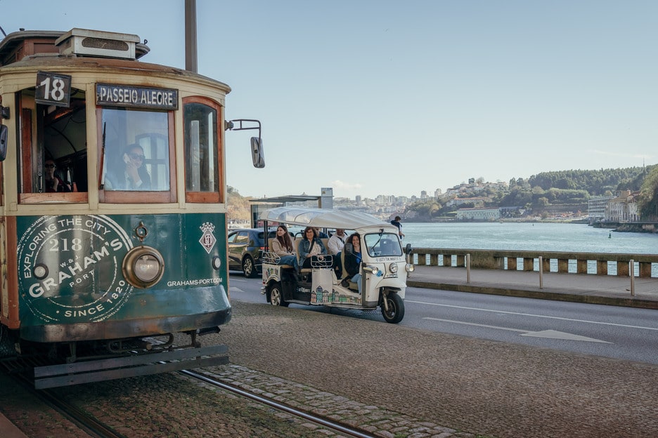 Tuk Tuk passing by historic tram on a scenic riverside street in Porto, Portugal