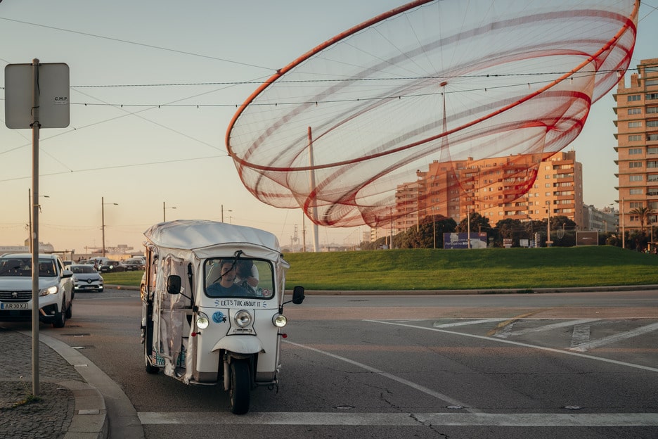 Tuk Tuk passing by the iconic She Changes sculpture in Porto, Portugal
